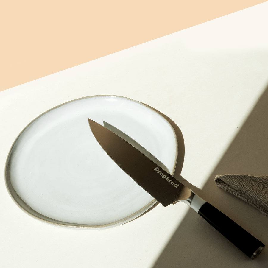 The chef knife resting on an organic shape plate, and prepared logo showing perfectly. The knife is in the color ,ash.