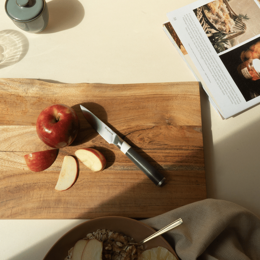  paring knife resting on a cutting board , cut apples, a breakfast oatmeal dish and a magazine