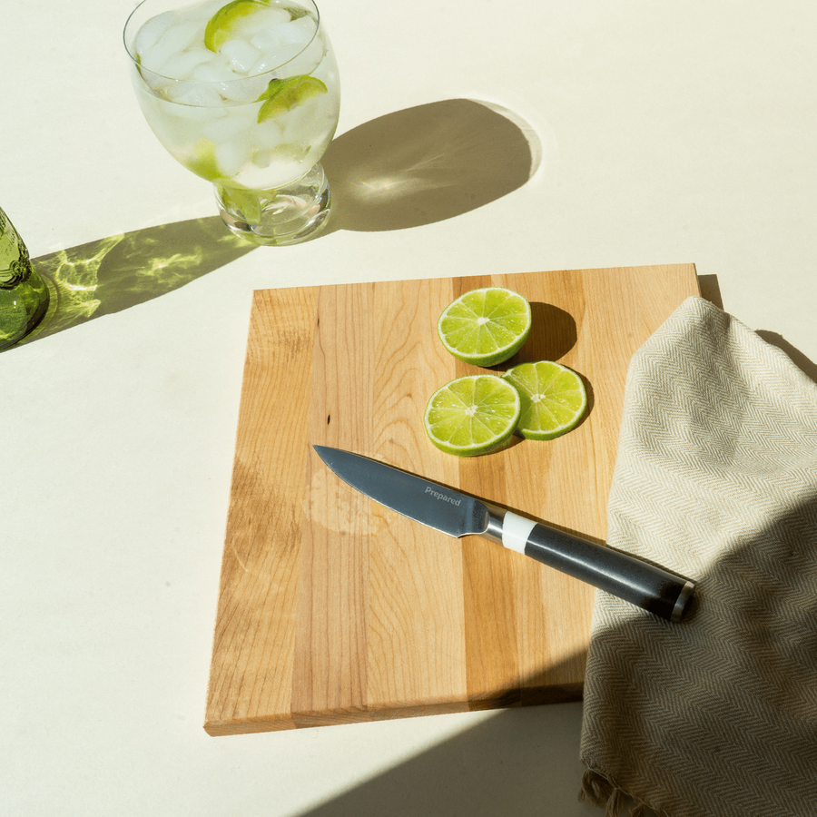 The ash colored paring knife resting on a cutting board, a cold glass of water with limes and thinly cut limes